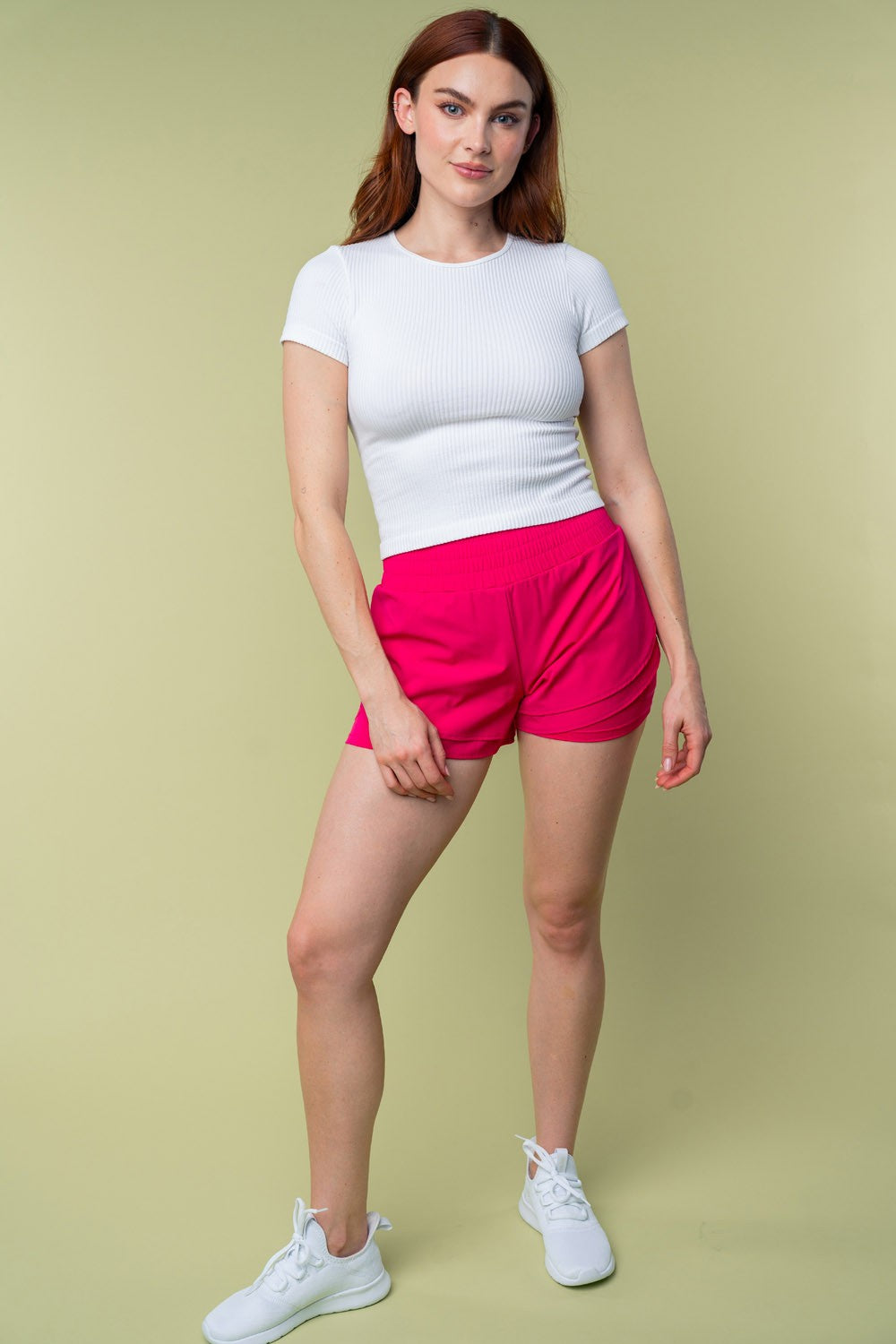 Model wearing White Birch pink high-waisted knit shorts paired with a white ribbed top and sneakers, styled for a casual look.