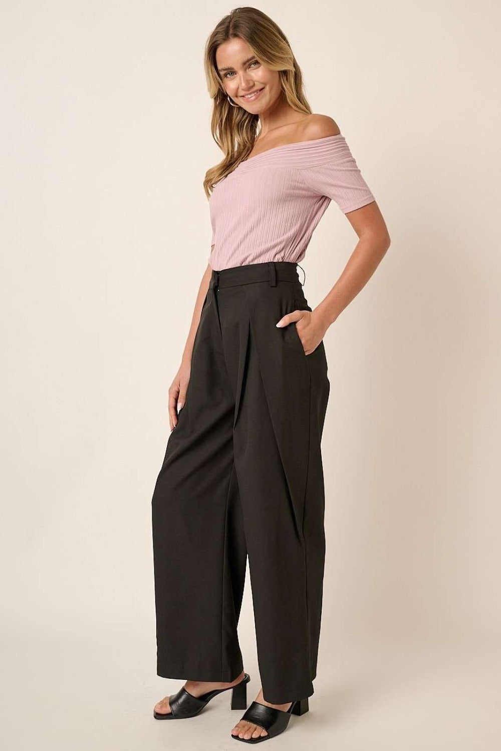 Mittoshop deep pleated high waisted wide leg pants styled with a pink off-shoulder top, shown in a side angle with hands in pockets.