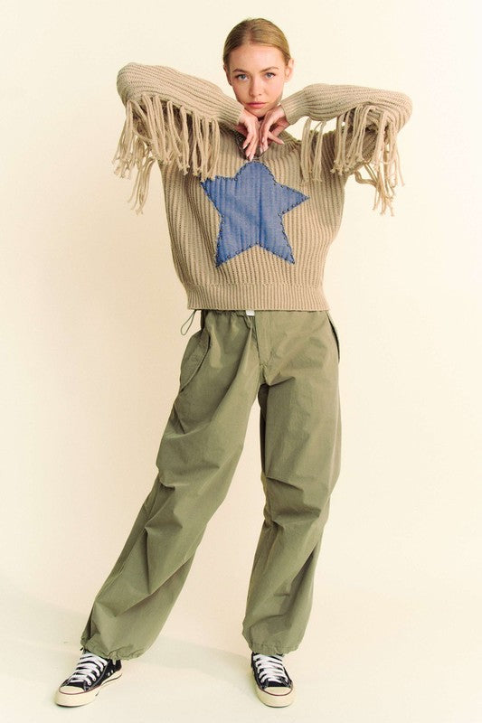 Model wearing Davi & Dani drawstring baggy pants with pockets in olive green, paired with a beige sweater featuring fringe details.