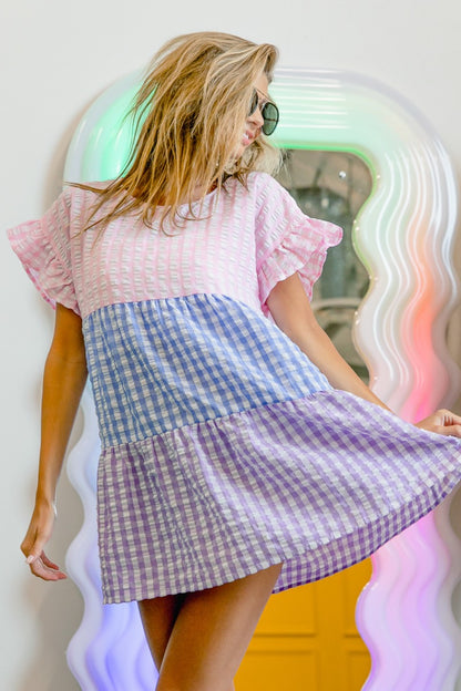 BiBi Plaid Color Block Tiered Top with pink, blue, and purple plaid tiers, featuring ruffle sleeves and a relaxed fit. Styled for a casual look.