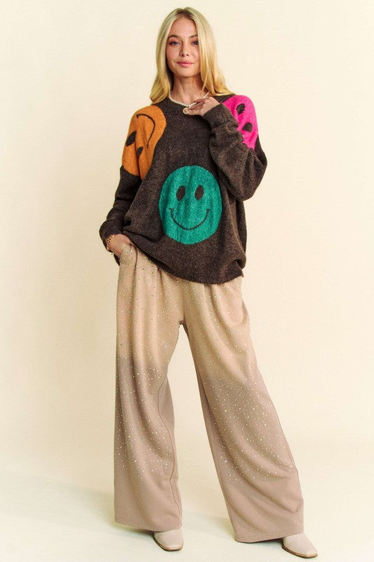 Model wearing Davi & Dani rhinestone drawstring wide-leg pants in beige paired with a colorful smiley sweater and white boots.